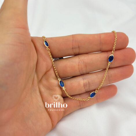 Foto mão mostrando detalhes da pulseira ajustável, sua cor é em ouro dourado e cristais azuis. Pulseira Rommanel revendida por Brilho Folheados. Código 551669