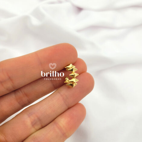 Foto fundo neutro, mão segurando brinco piercing losangos spike moderno folheado a ouro da marca Sabrina Joias. Código 1690509