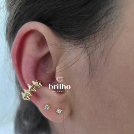 Foto orelha de modelo de pele clara usando brinco piercing de pressão losangos spike moderno folheado a ouro da marca Sabrina Joias. Código 1690509